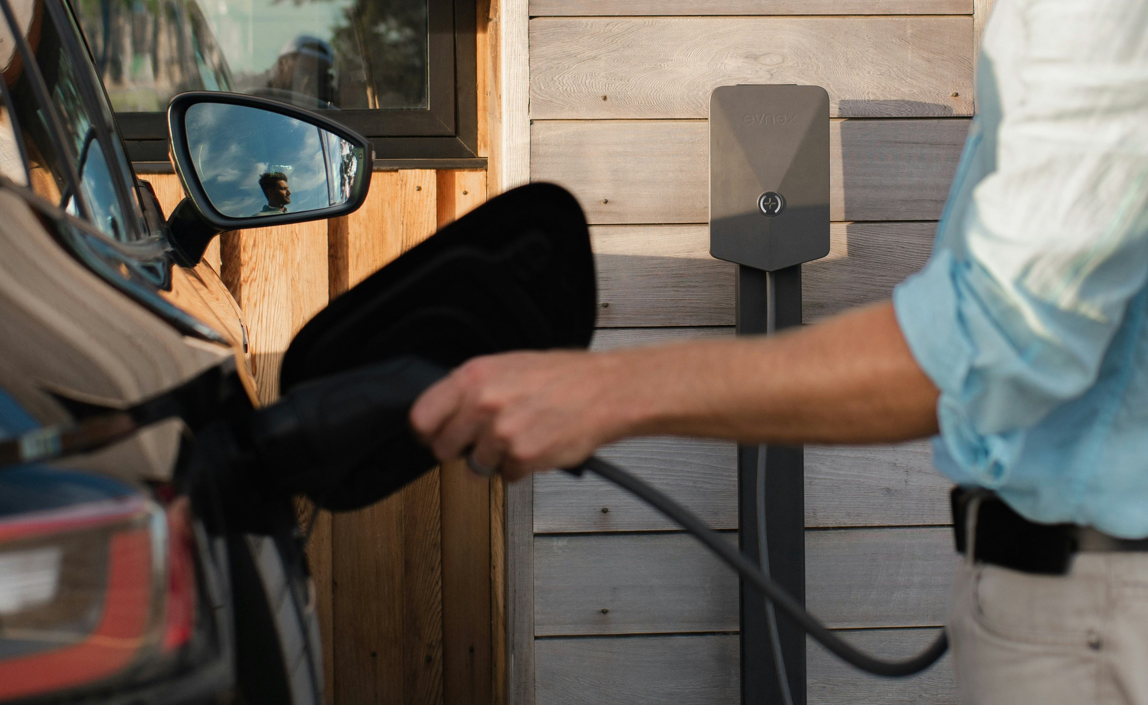 An EV being plugged into a home wall charger outside a timber-clad holiday let, with a branded GuestCharge graphic overlay reading "EV Charging for UK Holiday Lets — Complete 2026 Guide"